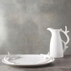 a white vase and plate sitting on a gray tablecloth with antlers in the background