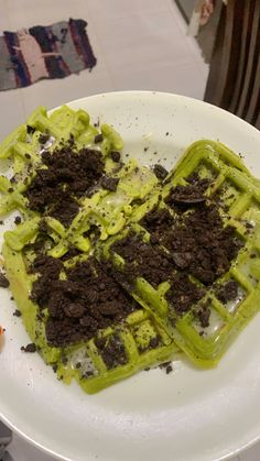 a white plate topped with waffles covered in green sauce and dirt on top of it