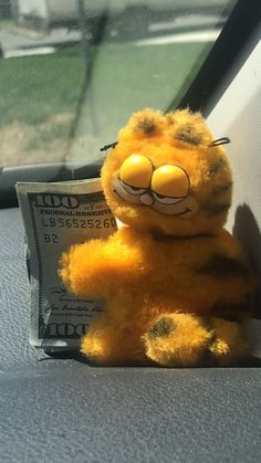 a yellow stuffed animal sitting on top of a car seat next to a pile of money