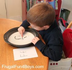 a little boy that is sitting at a table with a pan and paper on it