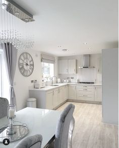 a large kitchen with white cabinets and wooden floors is pictured in this image, the dining room table has gray upholstered chairs