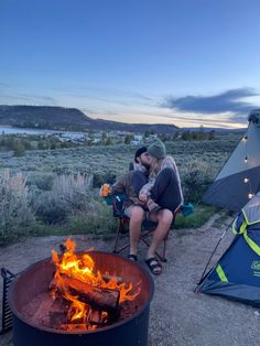 two people sitting in chairs next to a campfire