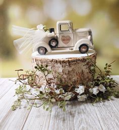 a wedding cake topper sitting on top of a tree stump with flowers around it