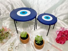 two blue tables with plants in them on a white cloth