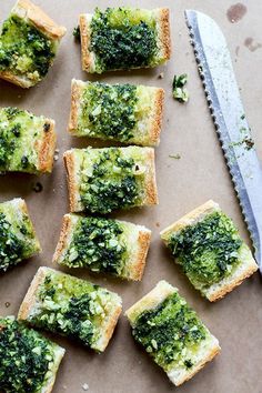 several pieces of bread with pesto on them next to a knife