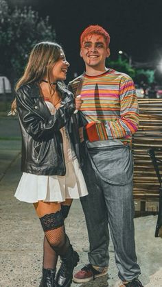 a man and woman standing next to each other in front of a bench at night