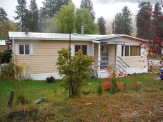 a mobile home sits in the middle of a grassy area with trees and shrubs around it