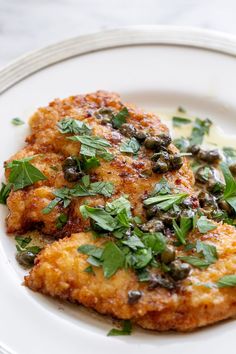 two pieces of fried chicken on a white plate with green garnish and parsley