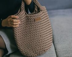 a woman sitting on a couch holding a brown knitted tote bag with two handles