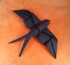 a black origami bird sitting on top of a brown table next to an orange wall