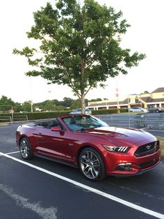 a red convertible car parked in a parking lot next to a tree and some buildings