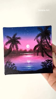 a hand holding up a small painting with palm trees and the moon in the background