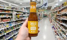 a person holding up a bottle of mild sauce in a store aisle with shelves full of food