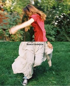 a woman in red shirt and white pants on grass