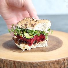 a hand is picking up a sandwich from a wooden plate on top of a tree stump