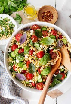 a white bowl filled with pasta salad next to wooden spoons