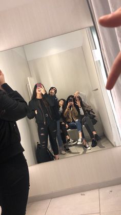 a woman taking a selfie in front of a mirror with other people behind her