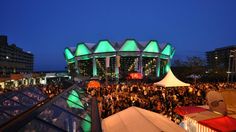 a crowd of people standing around tents in front of a large building with green lights