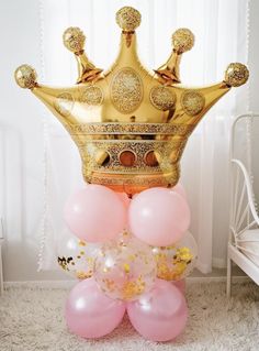 a gold crown sitting on top of balloons in front of a white bed and window