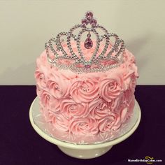 a pink cake decorated with roses and a tiara on top is sitting on a plate