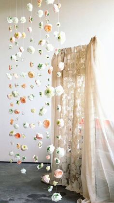 a room with curtains and flowers hanging from it's sides, in front of a window