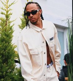 a man with dreadlocks standing in front of a tree wearing a white jacket