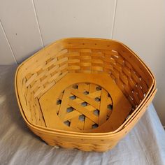 a wooden basket sitting on top of a white sheet covered table next to a wall