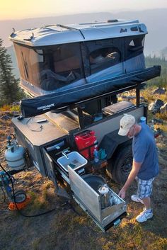 a man standing next to an open camper on top of a hill