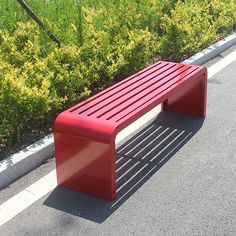 a red bench sitting on the side of a road next to bushes and shrubbery