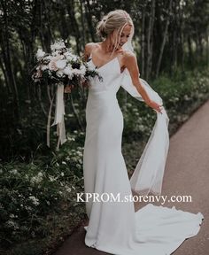 a woman in a white wedding dress is holding her veil over her shoulder and looking down at the ground