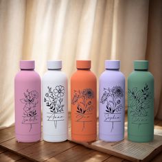 four different colored water bottles sitting on top of a wooden table