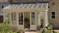 an orangery in the middle of a garden with potted plants