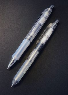 two pens sitting next to each other on top of a black surface with the same pen in it