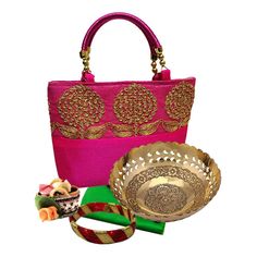 a pink purse with gold accents and other accessories including a small bowl, bracelets and ring