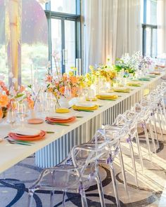 a long table is set up with clear chairs and colorful centerpieces on it