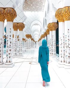 a woman in a blue hijab is walking through a hallway lined with columns