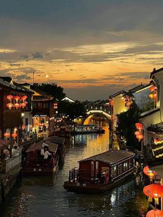 a river filled with lots of boats next to tall buildings at night time and lit up by lanterns