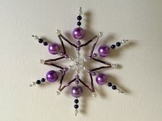 a purple and white snowflake with beads on it's side, hanging from a wall