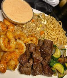 a plate full of food with shrimp, noodles and sauce on the side at a restaurant