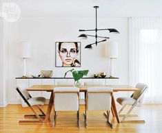 a dining room with white chairs and a wooden table in front of a painting on the wall