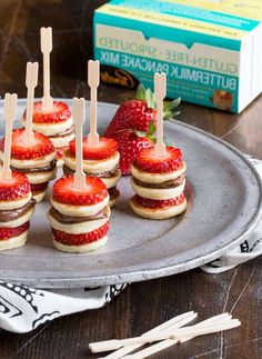 mini cheesecakes with strawberries are arranged on a silver platter next to a box of buttermilk pancakes