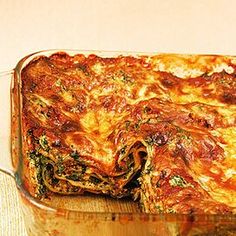 a casserole dish filled with lasagna and spinach on a wooden table