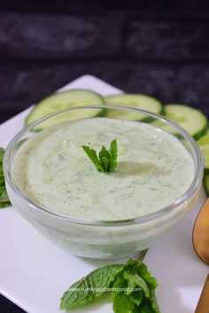 cucumber and mint dip in a glass bowl on a plate with spoons