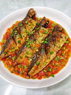 some fish are on a white plate with red sauce and green garnishes