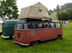 an old vw camper van with a tent on top parked in the grass