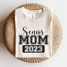 a white t - shirt with the words senior mom on it sitting next to a wicker basket