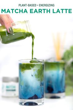 a person pouring green liquid into a glass filled with blue and green liquid on top of a white table