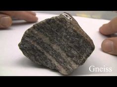 a rock being held by someone's hands on a white surface with the words gneiss above it