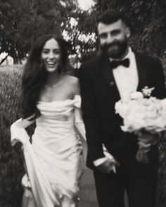 a black and white photo of a man and woman in formal wear walking down a path