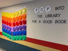 there is a colorful book cover on the wall in this school hallway that says pop into the library for a good book